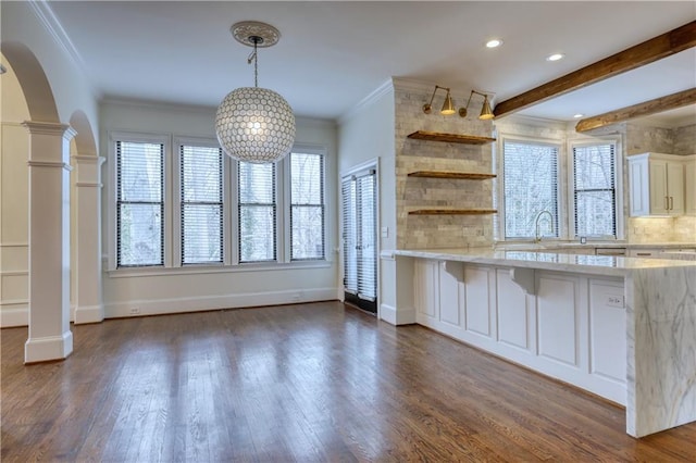 kitchen with a healthy amount of sunlight, decorative columns, arched walkways, and dark wood-style flooring