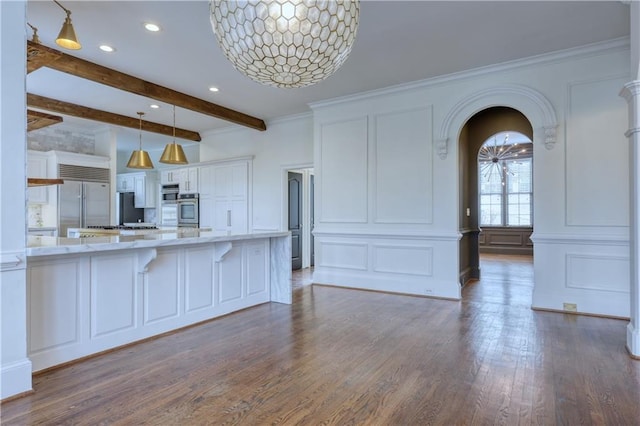 kitchen featuring arched walkways, light stone counters, a decorative wall, white cabinets, and beam ceiling