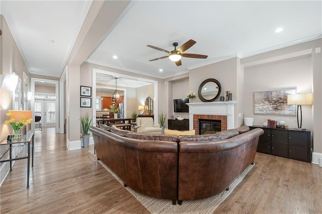 living room with a brick fireplace, ceiling fan, ornamental molding, and light hardwood / wood-style flooring