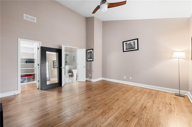 unfurnished bedroom featuring a walk in closet, light wood-type flooring, ceiling fan, high vaulted ceiling, and connected bathroom