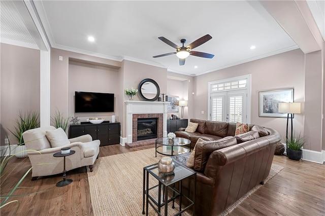 living room featuring ceiling fan, a fireplace, ornamental molding, and light wood-type flooring