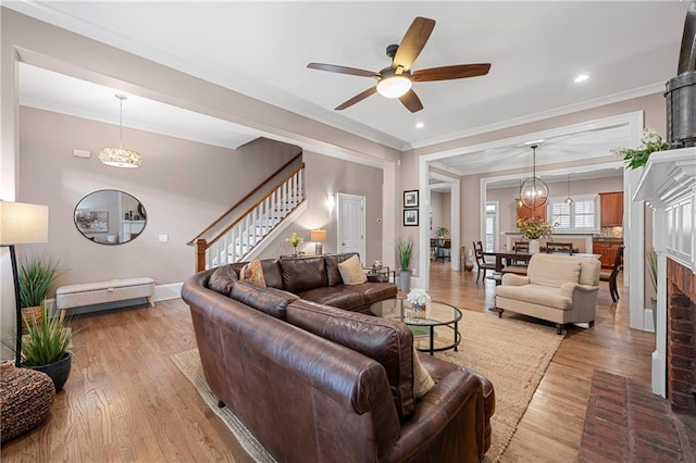 living room with a fireplace, ceiling fan with notable chandelier, light hardwood / wood-style floors, and ornamental molding