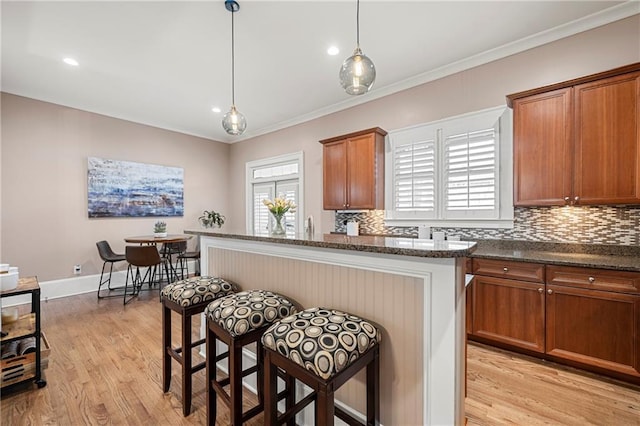 kitchen with a kitchen bar, crown molding, hanging light fixtures, and light wood-type flooring