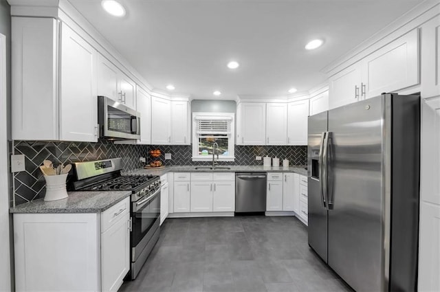 kitchen featuring sink, white cabinetry, stainless steel appliances, decorative backsplash, and dark stone counters