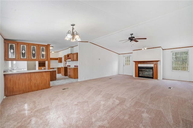 unfurnished living room featuring crown molding, lofted ceiling, light colored carpet, a tile fireplace, and ceiling fan with notable chandelier