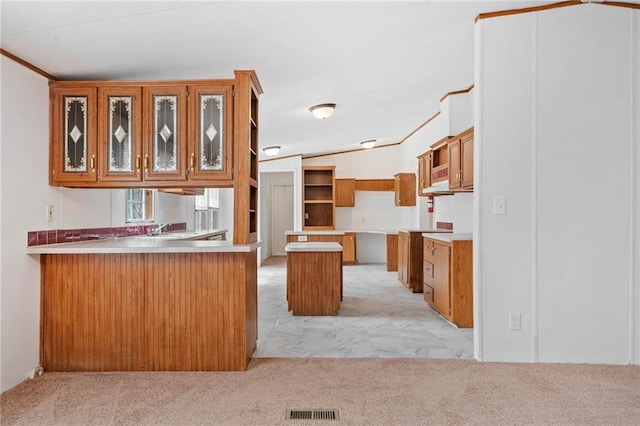 kitchen featuring visible vents, a kitchen island, glass insert cabinets, a peninsula, and light countertops