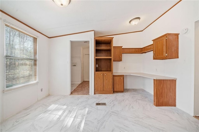 kitchen featuring visible vents, light countertops, brown cabinets, built in desk, and crown molding