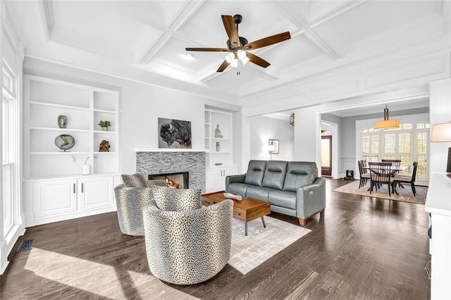 living area featuring a lit fireplace, coffered ceiling, dark wood finished floors, and built in features