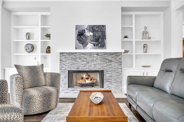 living area featuring built in features, dark wood-type flooring, and a stone fireplace