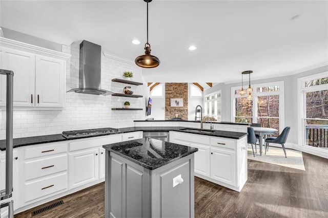 kitchen featuring dark wood-style floors, wall chimney exhaust hood, a peninsula, stainless steel appliances, and a sink