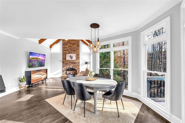 dining room featuring a fireplace, wood finished floors, baseboards, vaulted ceiling, and ornamental molding