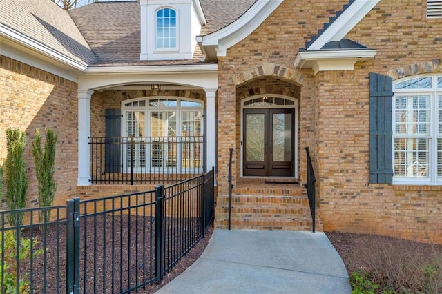 view of exterior entry featuring brick siding, a shingled roof, and french doors