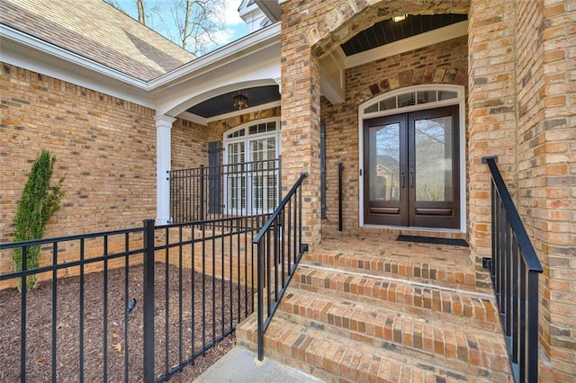 entrance to property featuring a shingled roof, french doors, and brick siding