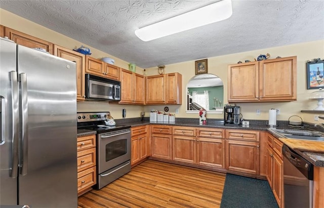 kitchen featuring appliances with stainless steel finishes, sink, a textured ceiling, and light hardwood / wood-style flooring