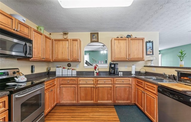 kitchen featuring appliances with stainless steel finishes, sink, light hardwood / wood-style flooring, and a textured ceiling