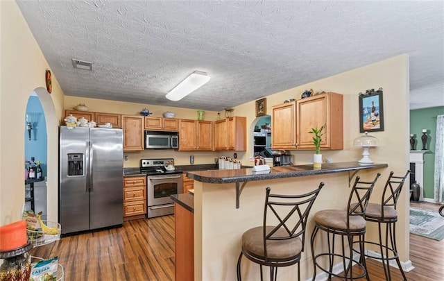 kitchen with stainless steel appliances, wood-type flooring, a breakfast bar, and kitchen peninsula