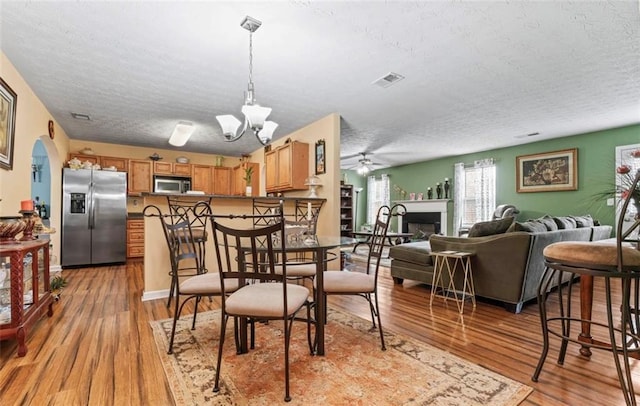 dining room with ceiling fan with notable chandelier, a textured ceiling, and light hardwood / wood-style floors