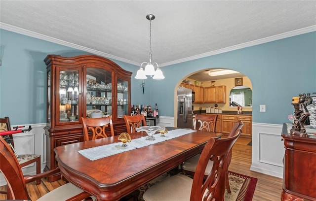 dining area with ornamental molding, a textured ceiling, an inviting chandelier, and light hardwood / wood-style flooring