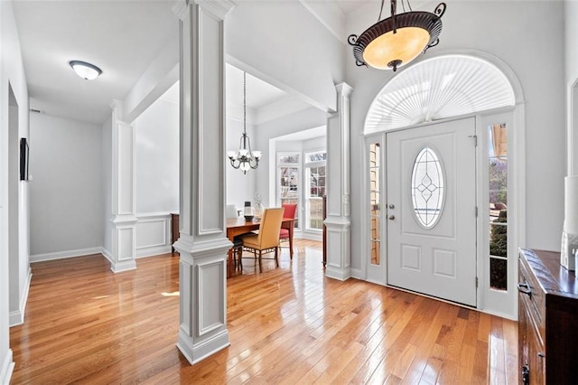 entryway with an inviting chandelier, light wood-style flooring, baseboards, and ornate columns