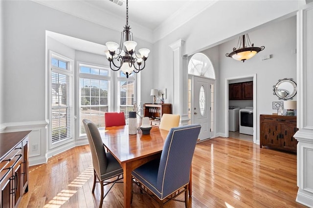 dining area with washing machine and clothes dryer, light wood-type flooring, ornamental molding, a notable chandelier, and ornate columns