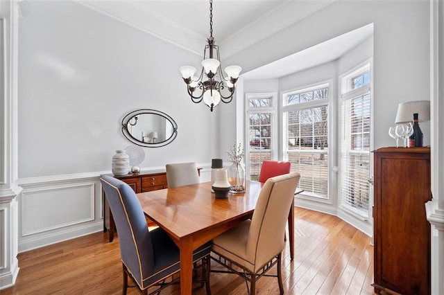 dining room featuring a wainscoted wall, a notable chandelier, light wood-style floors, crown molding, and a decorative wall