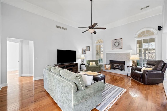 living room with light wood finished floors, visible vents, a brick fireplace, and baseboards