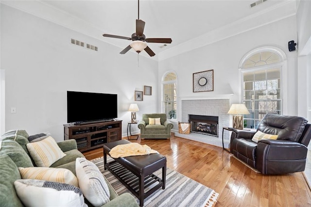 living area with visible vents, light wood-style floors, a brick fireplace, and ceiling fan