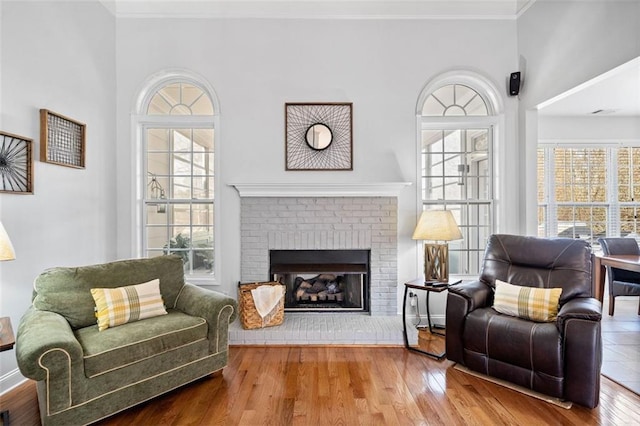 living room with a healthy amount of sunlight, a brick fireplace, wood finished floors, and ornamental molding