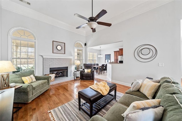 living room with ceiling fan, wood finished floors, a fireplace, and crown molding