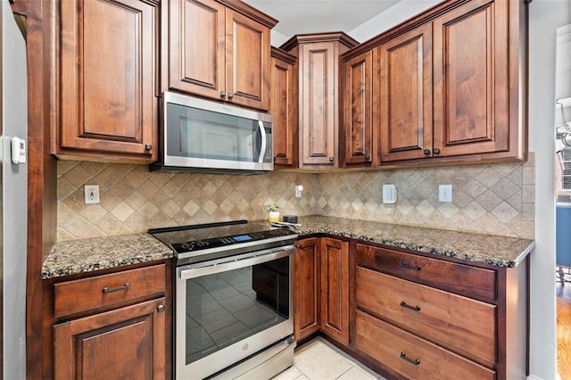 kitchen featuring backsplash, light tile patterned floors, dark stone countertops, appliances with stainless steel finishes, and brown cabinets