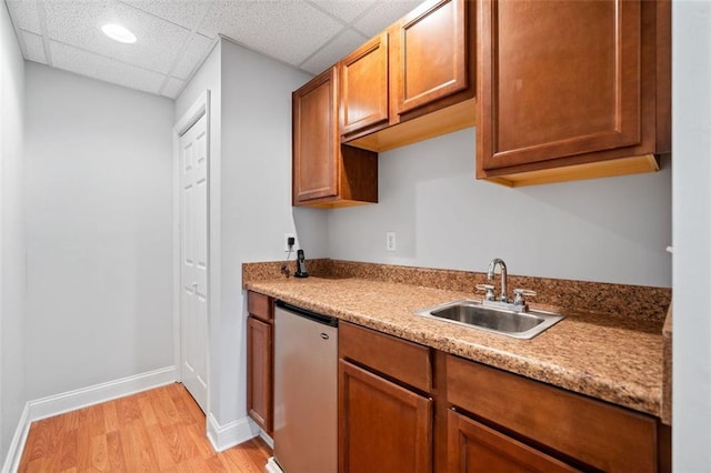 kitchen with light wood-style flooring, a sink, brown cabinetry, baseboards, and dishwasher