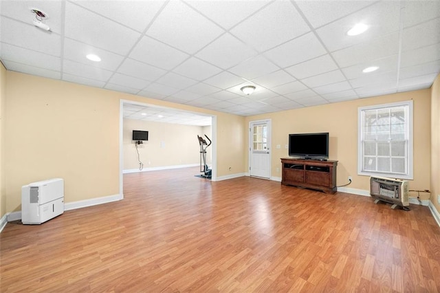 unfurnished living room featuring a drop ceiling, heating unit, baseboards, and light wood finished floors