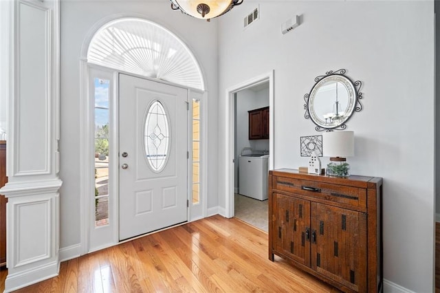 entryway with washer / dryer, baseboards, visible vents, and light wood finished floors