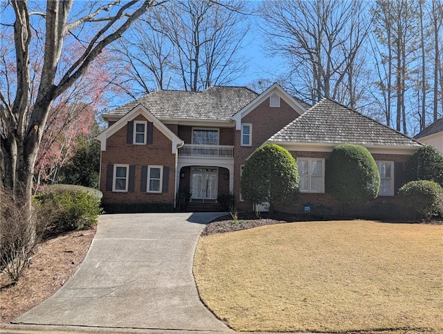 traditional home with driveway, brick siding, a front yard, and a balcony