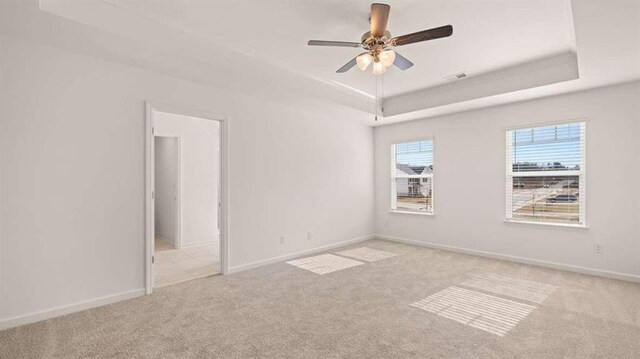 spare room with a raised ceiling, ceiling fan, and light colored carpet