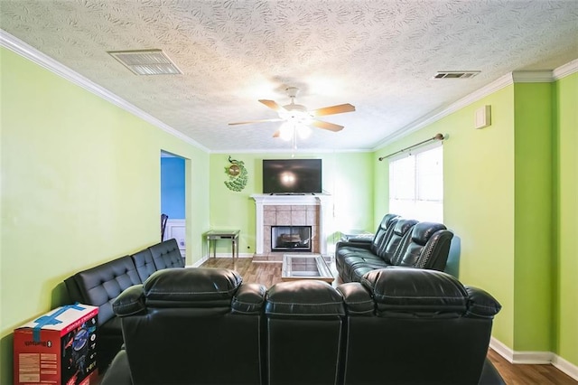 living room featuring a tile fireplace, hardwood / wood-style floors, a textured ceiling, and crown molding