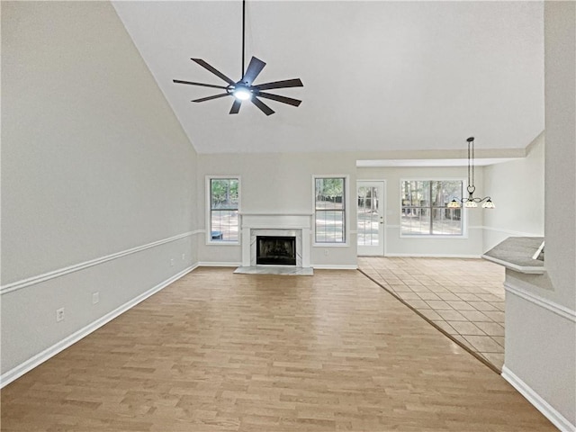 unfurnished living room with light hardwood / wood-style floors, high vaulted ceiling, a premium fireplace, and ceiling fan with notable chandelier