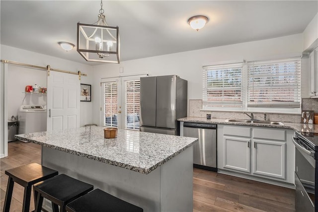 kitchen with sink, a barn door, pendant lighting, stainless steel appliances, and washer / clothes dryer