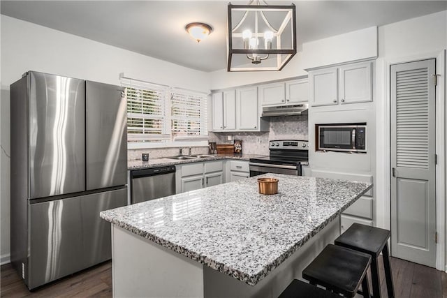 kitchen with a kitchen island, appliances with stainless steel finishes, pendant lighting, decorative backsplash, and light stone counters