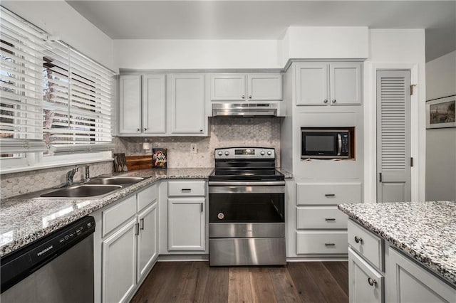 kitchen with dark wood-type flooring, sink, light stone counters, stainless steel appliances, and backsplash