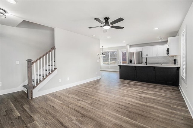 unfurnished living room with ceiling fan with notable chandelier and dark wood-type flooring