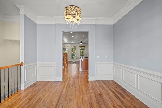 unfurnished dining area with crown molding, sink, ceiling fan with notable chandelier, and light wood-type flooring