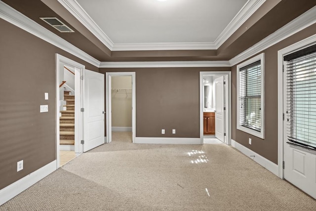 unfurnished bedroom with ensuite bath, a walk in closet, light colored carpet, and ornamental molding