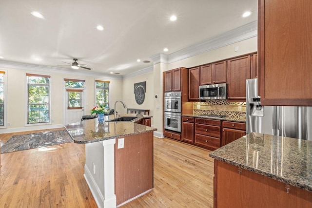 kitchen featuring sink, dark stone counters, light wood-type flooring, appliances with stainless steel finishes, and ornamental molding