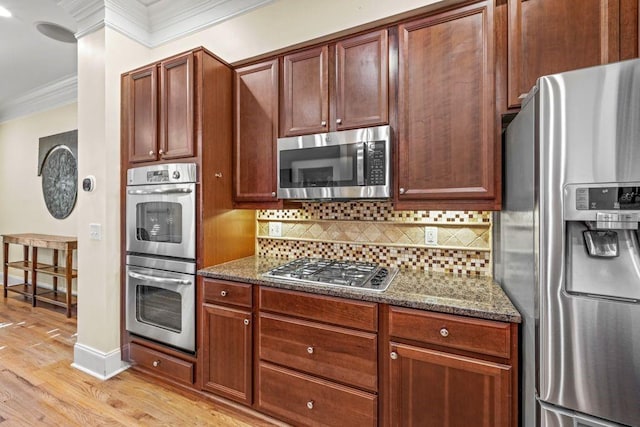 kitchen with dark stone counters, ornamental molding, tasteful backsplash, light hardwood / wood-style floors, and stainless steel appliances