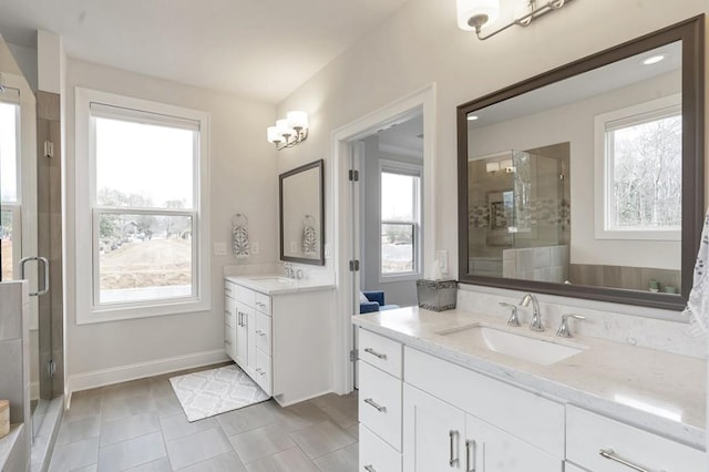 full bath with a stall shower, two vanities, a sink, and baseboards