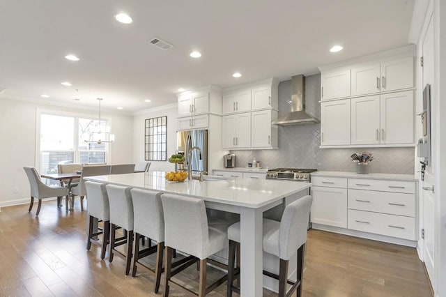 kitchen with tasteful backsplash, visible vents, ornamental molding, a sink, and wall chimney exhaust hood