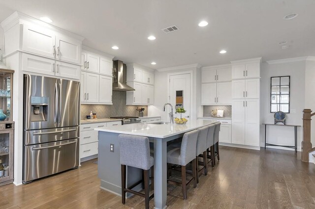 kitchen with stainless steel appliances, visible vents, white cabinets, a sink, and wall chimney exhaust hood