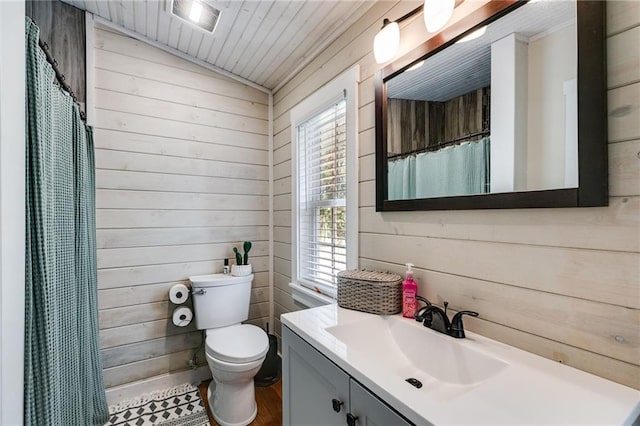 bathroom with lofted ceiling, vanity, wooden walls, and toilet