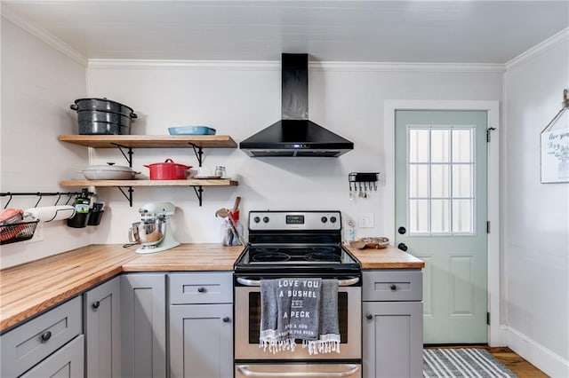 kitchen with butcher block countertops, gray cabinets, wall chimney range hood, and electric stove